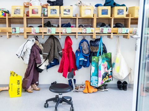 Leikskólaföt hangandi á snögum við hólf barna á leikskóla.