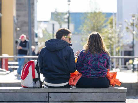 Tvær manneskjur sitja saman á bekk.