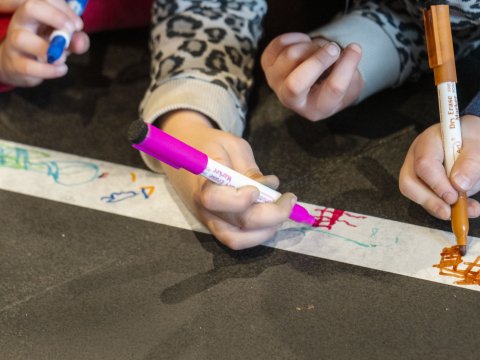 Nærmynd af höndum barna að teikna á hvítan renning