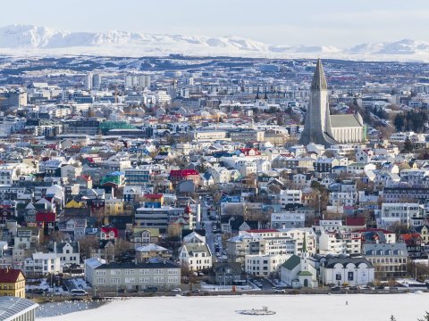 Aerial view of Reykjavík in winter. Snow, white mountains in the background, Hallgrímskirkja on the right side of the frame in the center, Tjörnin in the foreground.