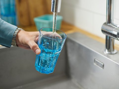 Vatn rennur úr krana í glas sem haldið er undir vatnsbununni