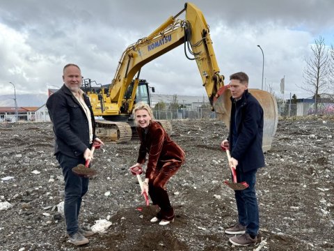 Tveir karlmenn og ein kona taka skóflustungu og bak við þau er grafa