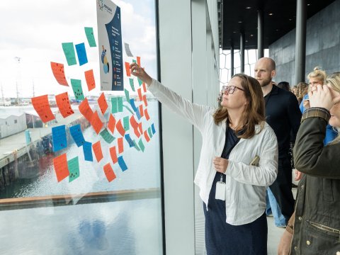 Kona setur post-it miða á glugga í Hörpu en þannig var hugmyndum safnað saman vegna nýrrar aðgerðaáætlunar velferðarstefnu Reykjavíkurborgar