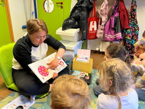 Mynd af starfsmanni leikskóla sýna börnum myndir í bók.