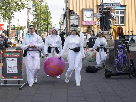 Young people in white overalls carrying a large pink ball walk down Bankastræti. Street art hosted by Hitt Húsið Youth Center.