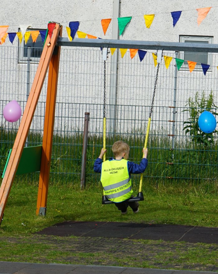 Barn að róla sér í gulu vesti á leikskólanum Hraunborg. Blöðrur og fánar í kringum róluna.