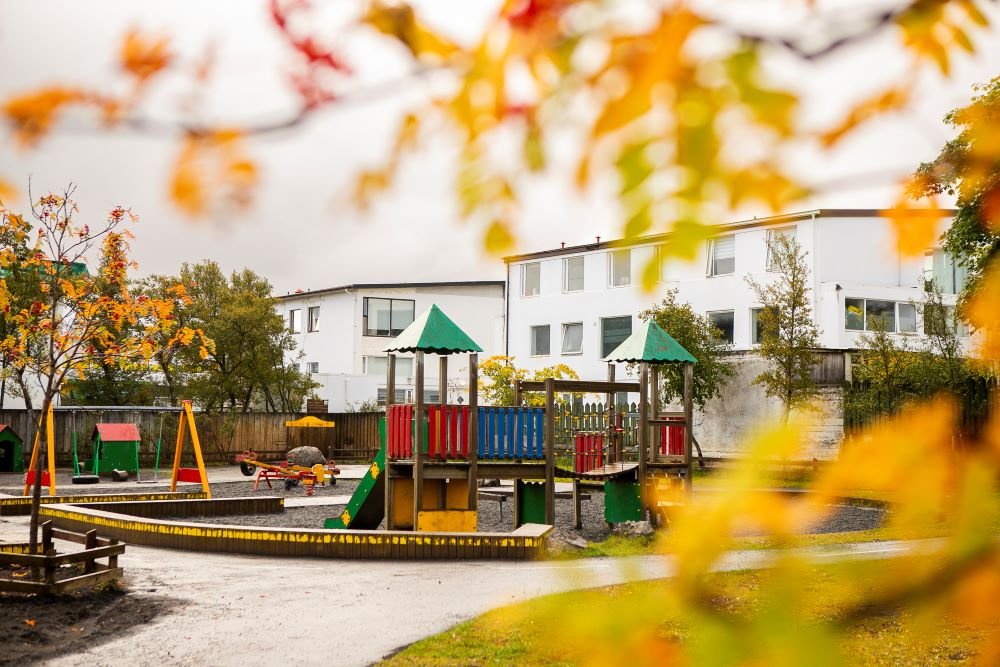 Leikkastali, rólur og vegasalt á útisvæði leikskólans Björtuhlíðar. Laublöð í forgrunni.