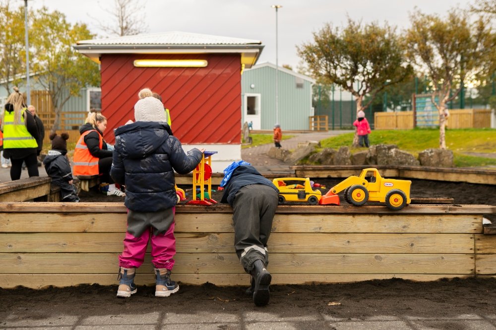 Börn í útigöllum að leika sér við sandkassa á útisvæði leikskólans Gullborgar