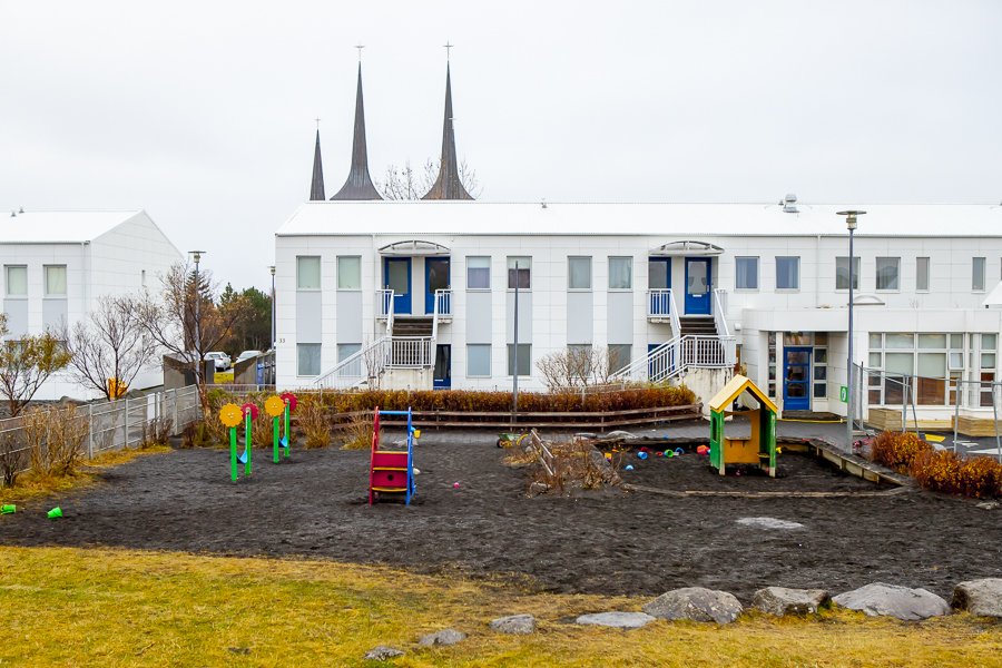 Outdoor playground equipment at Klambrar preschool. The white preschool building in the background with the towers of Háteigskirkja church.
