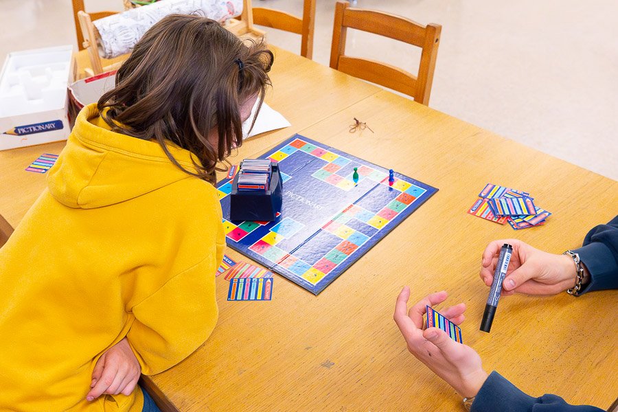 Children sit at table playing cards. 