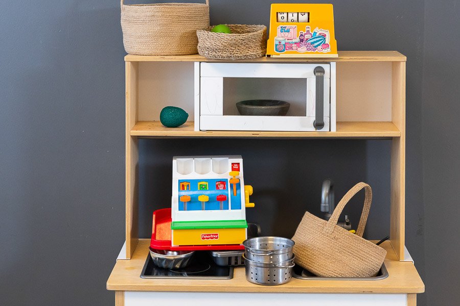A toy kitchen with a microwave and stovetop along with a toy cash register.