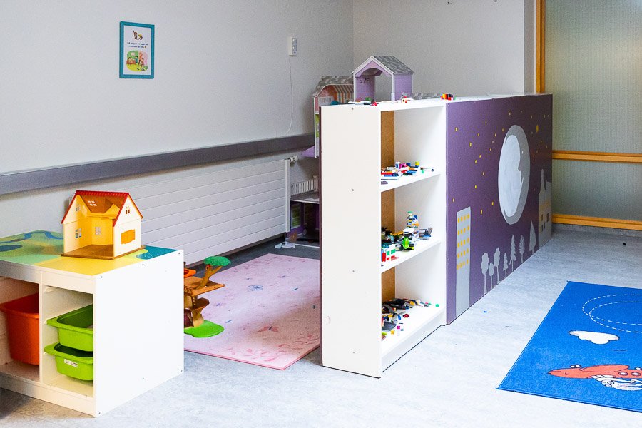 Play area at Eldflaugin after-school program with colorful rugs, shelves with Lego blocks and a dollhouse.