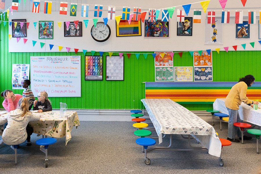 Dining room at the Frostheimar after-school program with green painted walls, posters, a clock and Rainbow Flag on the wall, and flag strings hanging from the ceiling.