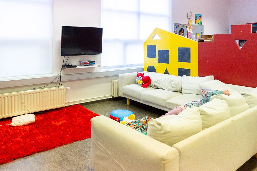 A child lying on a sofa in front of a television. A red rug on the floor. 