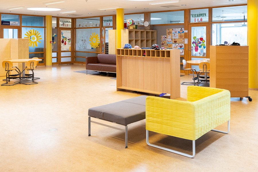 Hall with tables and chairs, yellow sofas and shelves at Laugarsel after-school program. 