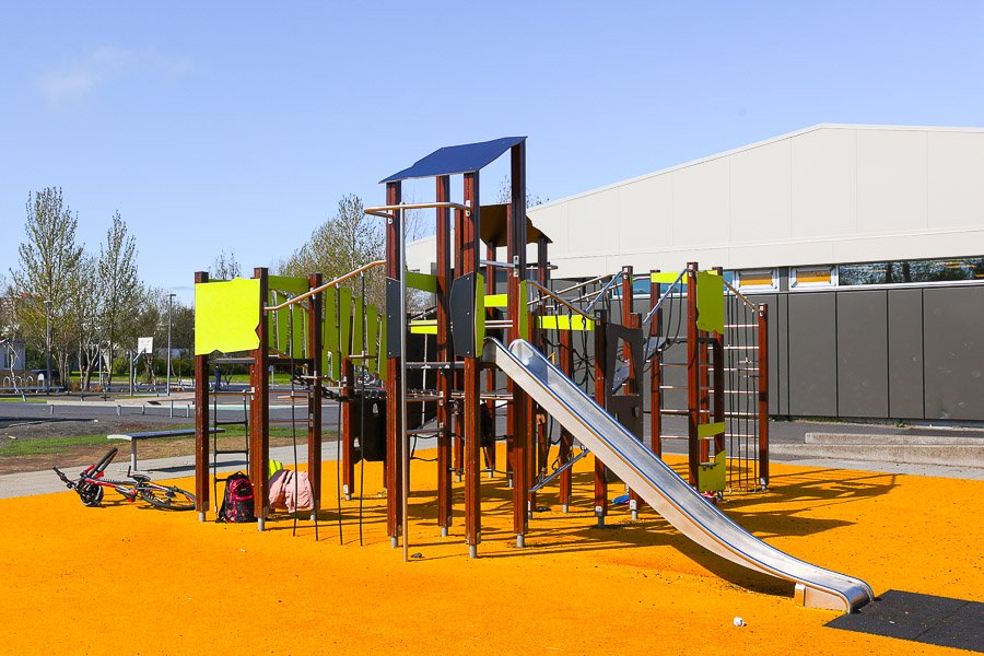 Playground castle with slide and climbing frame on orange flooring.