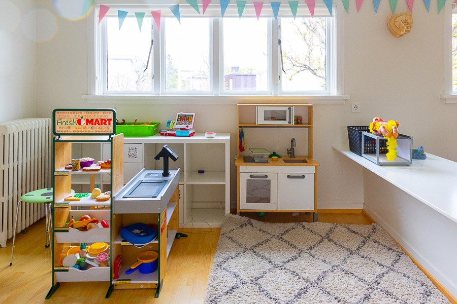 Room with a toy kitchen, rug on the floor and bunting in the window.