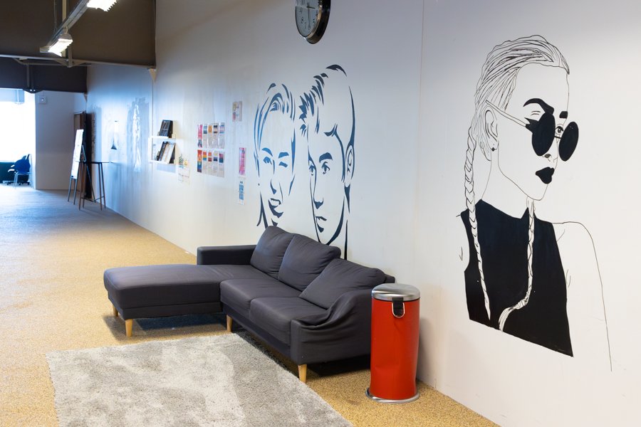 Gray sofa, light area rug, and red trash bin. Pictures of celebrities in black-and-white are painted on the wall behind.