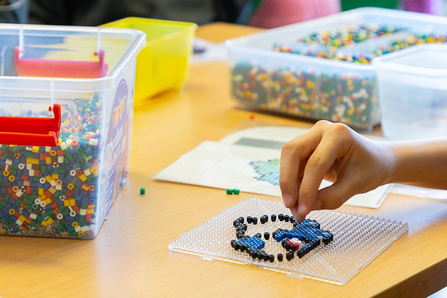 Perler beads on a table and a child's hand making beadwork.