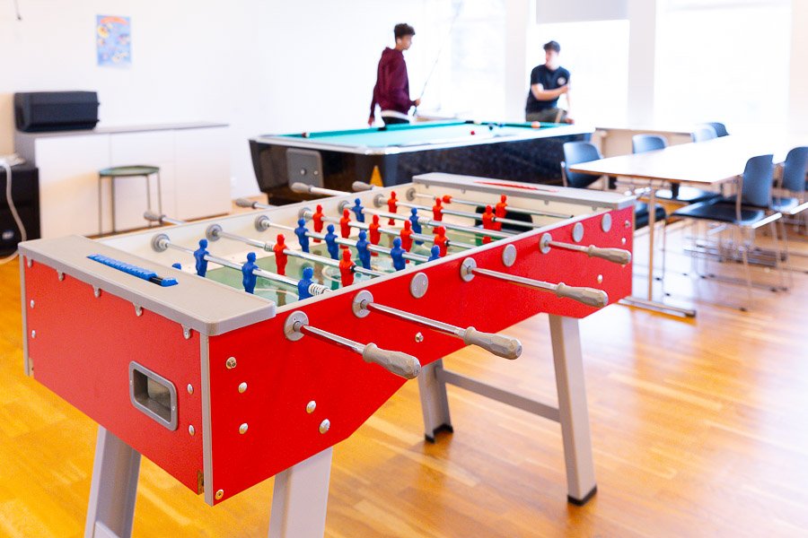 Room with a foosball table and pool table. Teenagers playing pool. 