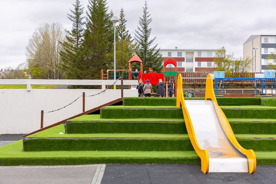 Steps with artificial grass and a slide. Playground equipment in the background. 