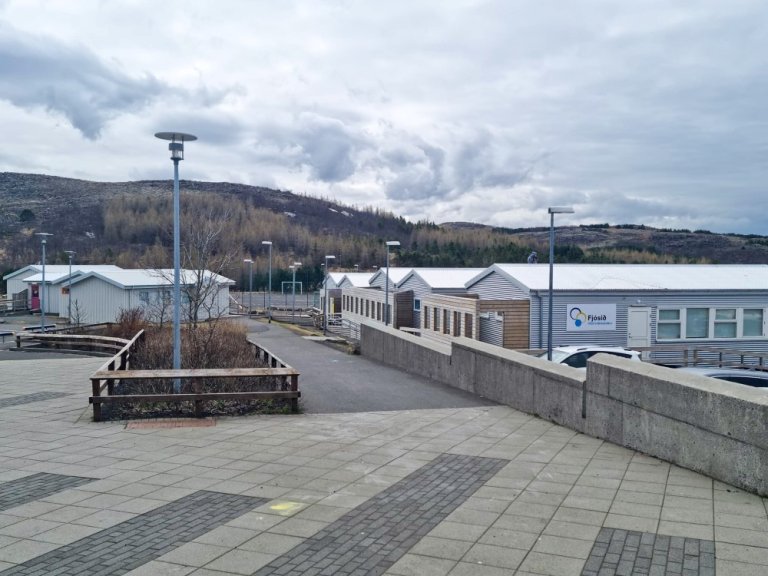 Hvít, lágreist hús sem standa í röðum. Stétt fremst á mynd og ljósastaurar.