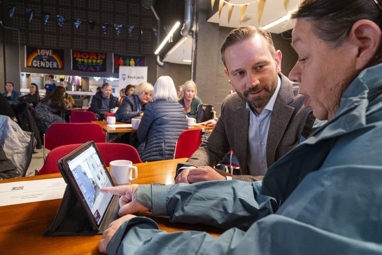 Mayor Einar Þorsteinsson looks on as a woman shows him information on a tablet at a resident forum in Miðborg.