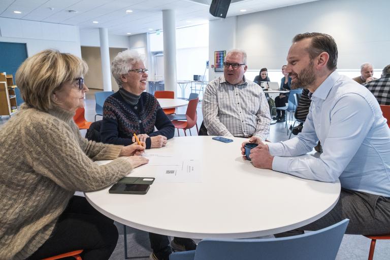 Mayor Einar Þorsteinsson sits at a table with three older residents at a resident forum at Vesturbæjarskóli.
