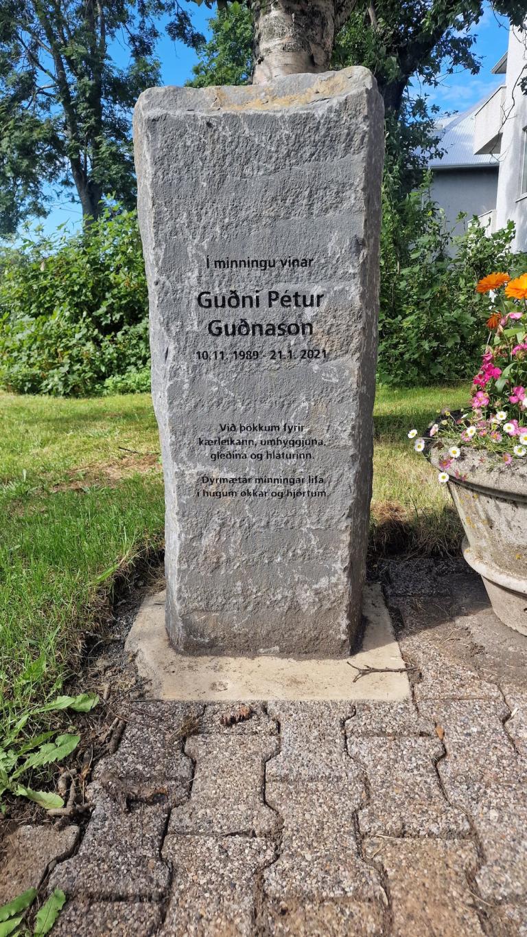 Minningarsteinn um Guðna Pétur sem stendur við hlið gróðurhússins sem var reist í hans minningu.