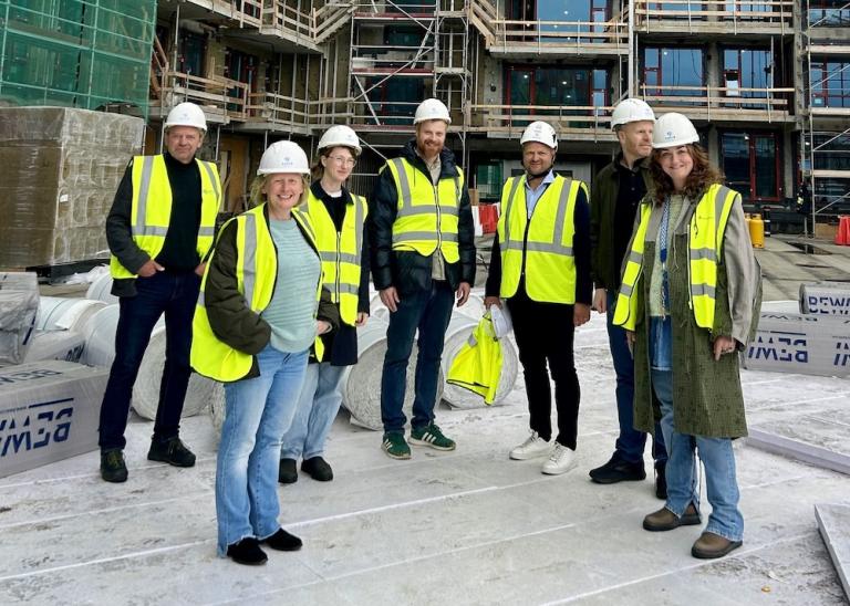fólk í vinnufötum með hjálm og blokk í byggingu í baksýn