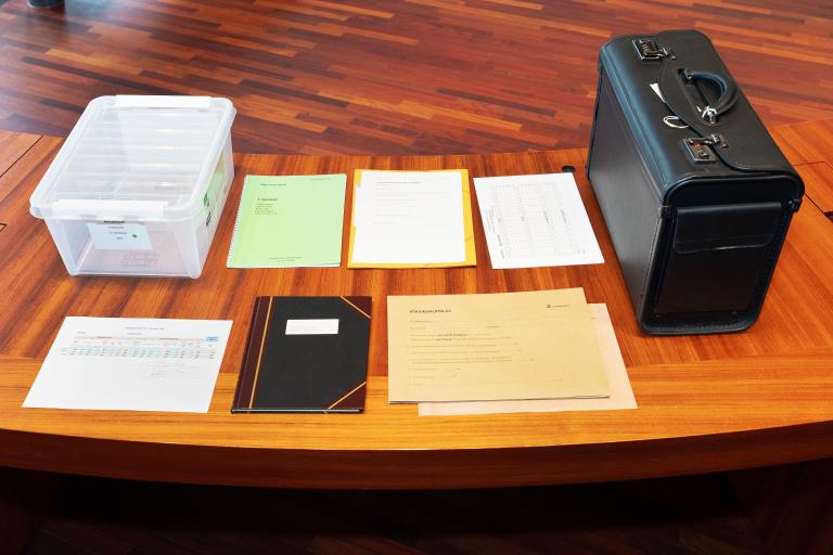Municipal election materials arranged on a table at City Hall. A clear box, paperwork, and a black document bag.