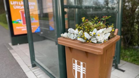 Brún tunna full af gróðri við strætóskýli