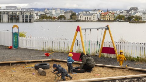 Börn í sandkassa með rólur í baksýn á útisvæði leikskólans Tjarnar