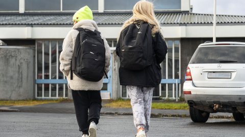 Skólakrakkar að ganga í skólann með skólatöskur á bakinu.