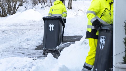Tveir starfsmenn sorphirðu draga tunnur merktar borginni, snjór úti.