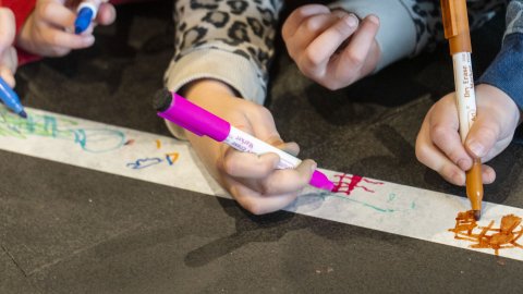 Nærmynd af höndum barna að teikna á hvítan renning