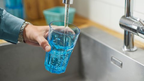 Vatn rennur úr krana í glas sem haldið er undir vatnsbununni