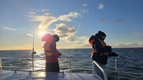Tveir krakkar í björgunarvestum með veiðistangir á veiðum úti á sjó.